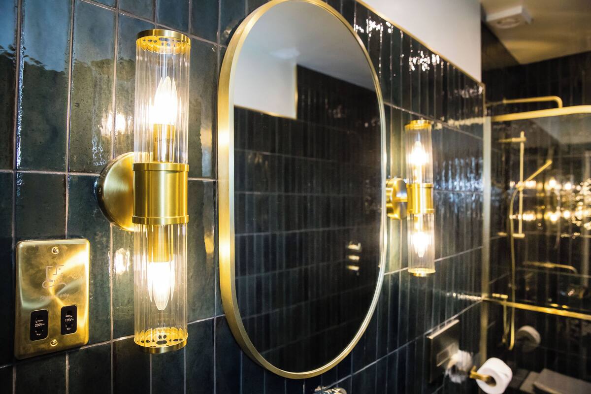 A bathroom with a large mirror, wall-mounted lights, and a towel rack.