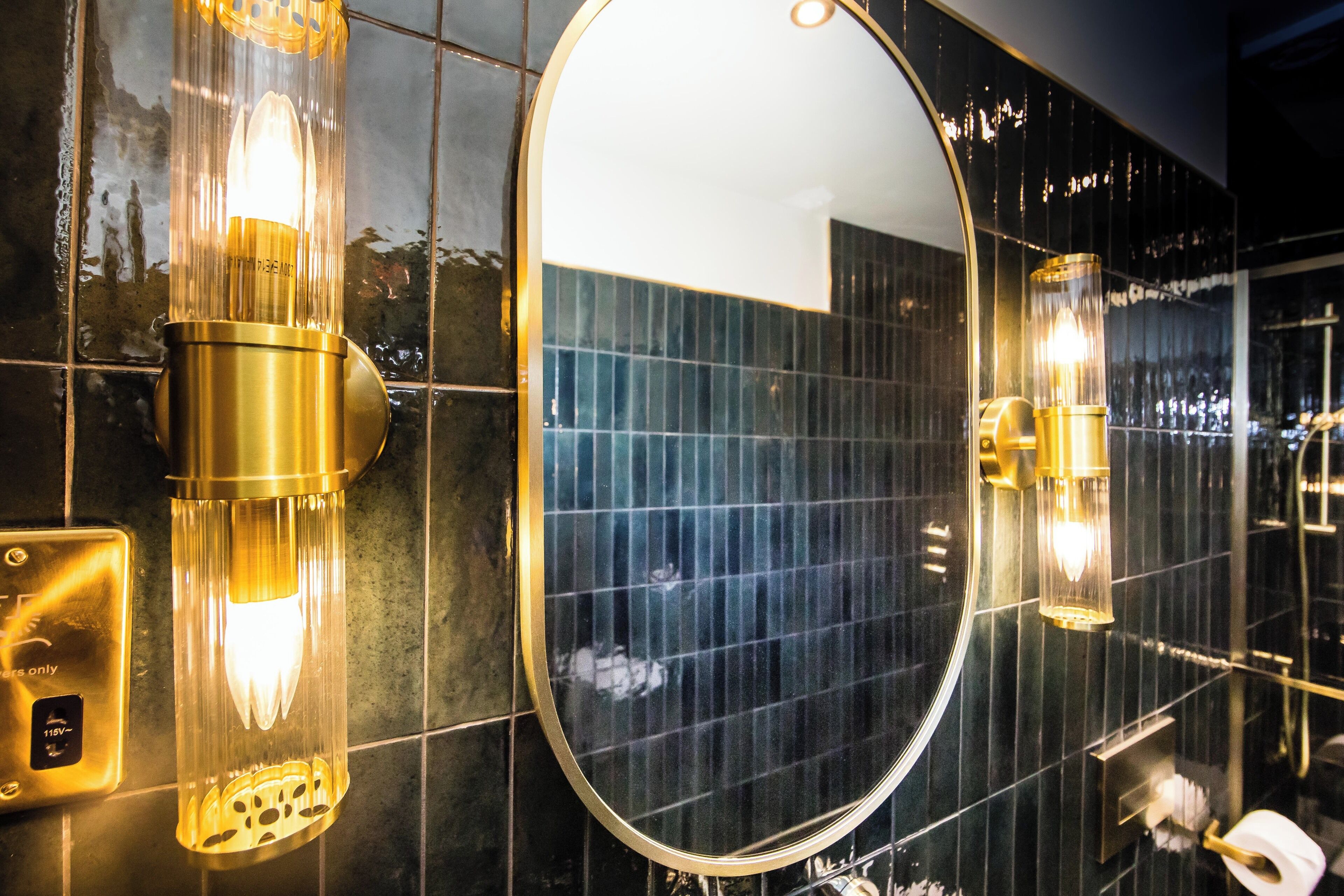 Un baño con un espejo ovalado grande, dos luces fijadas a la pared y un inodoro.