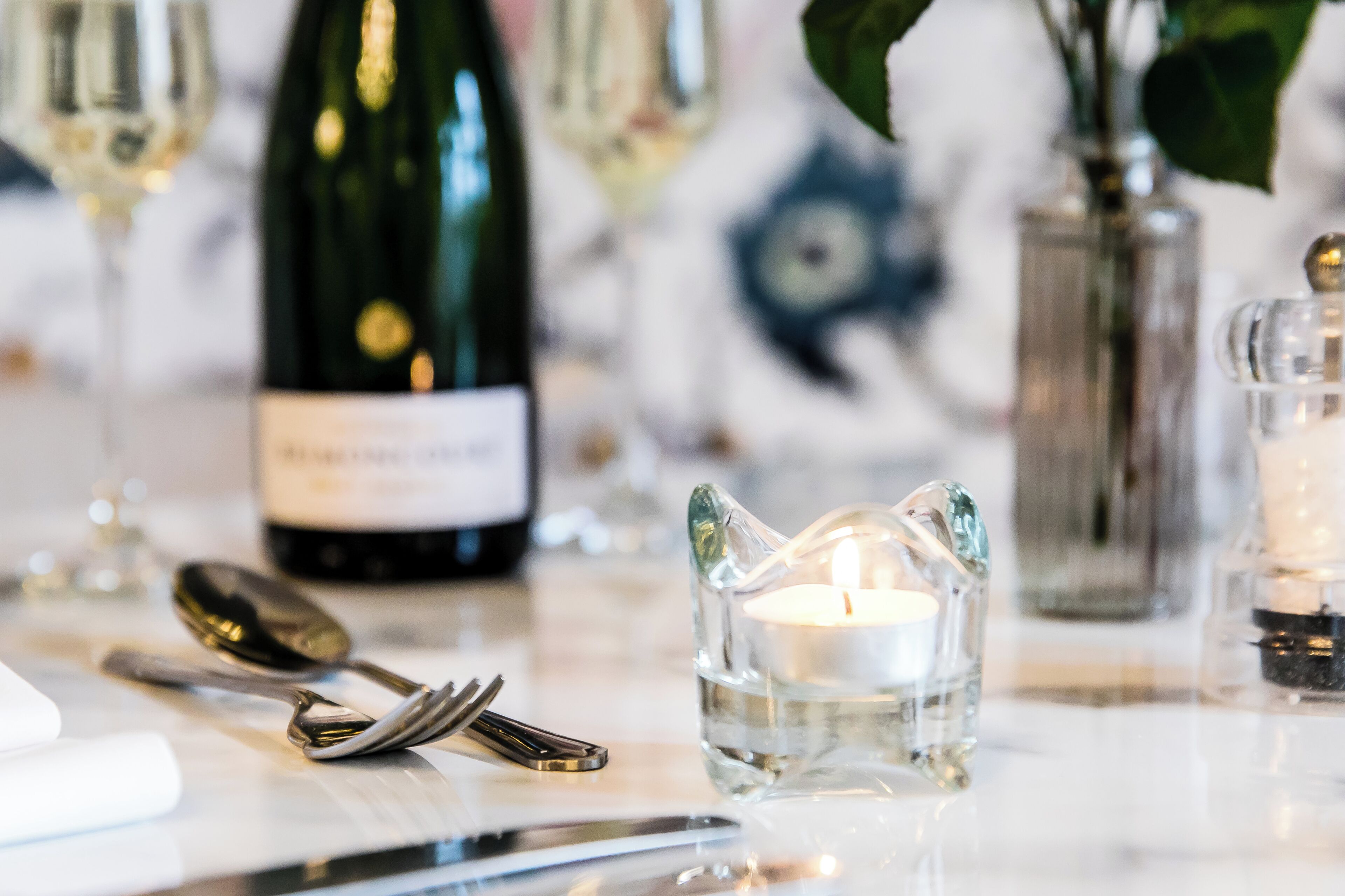 A table setting with a wine bottle, a candle in a glass holder, and cutlery.