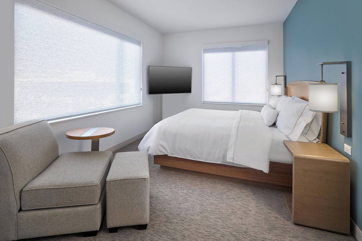 A hotel room with a bed, a sofa, a small table, a TV, and a lamp.