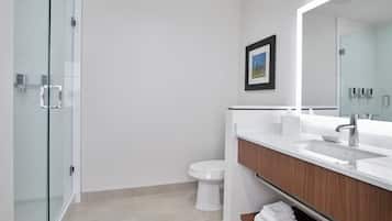 A modern bathroom with a glass shower enclosure, a white toilet, a large mirror, and a wooden vanity with a sink.