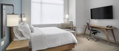 A modern hotel room with a bed, desk, chair, TV, and bedside lamps.