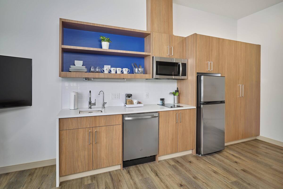 A modern kitchen with wooden cabinets, a stainless steel refrigerator, a microwave, and a dishwasher.