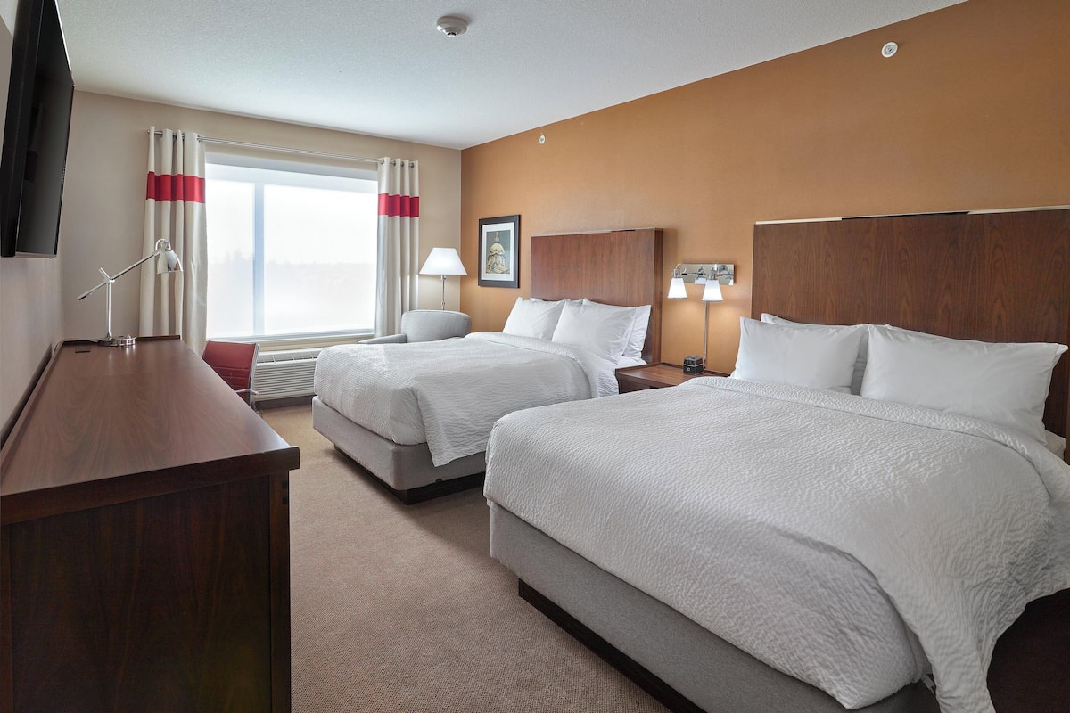 A hotel room with two beds, a desk, a TV, and a window with curtains.