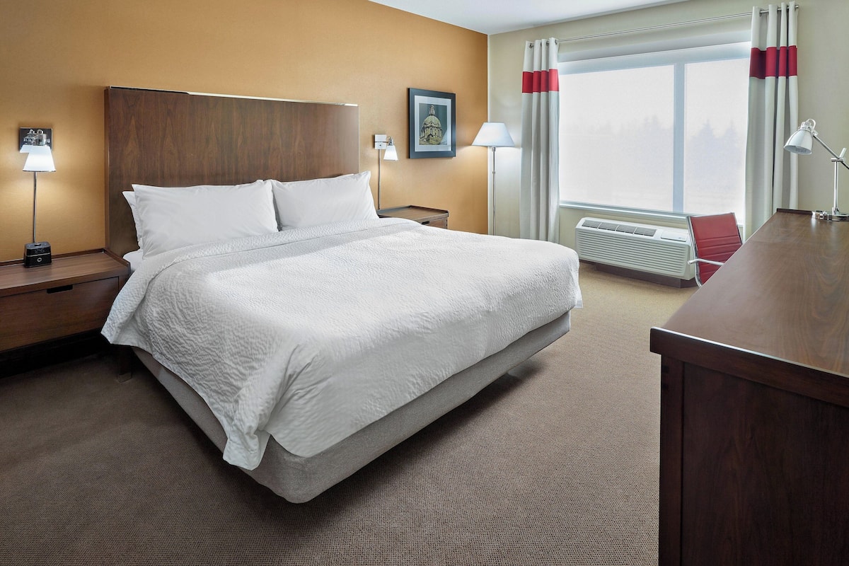 A hotel room with a large bed, bedside lamps, a nightstand, a desk, and a window with curtains.