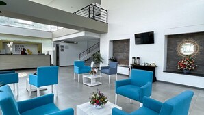 Un vestíbulo amplio con sillas modernas de color azul, una mesa de centro blanca y un mostrador de recepción.