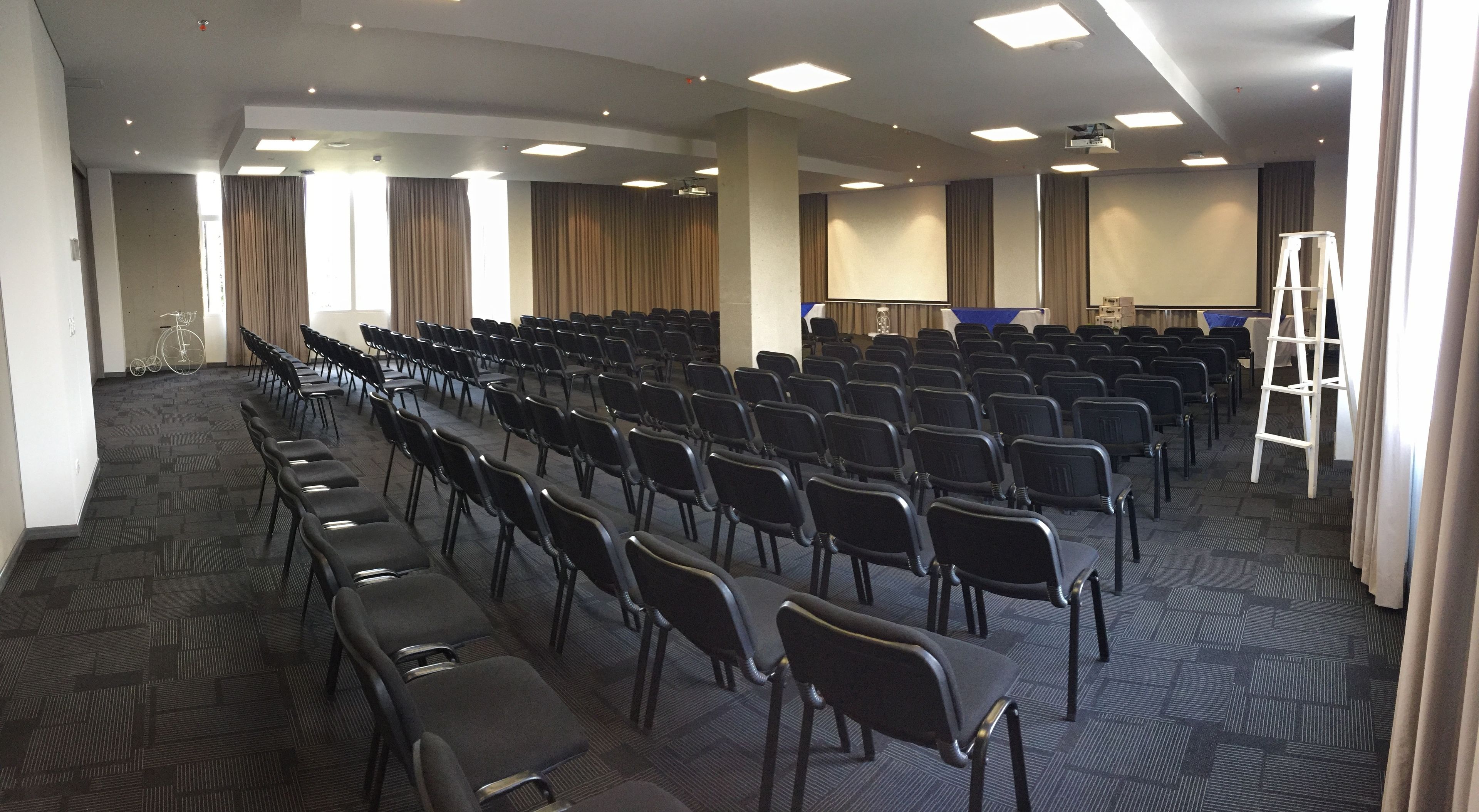 A conference room with rows of chairs, a projector screen, and a white ladder.