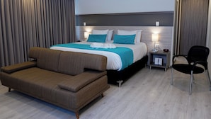 Una habitación de hotel moderna con una cama grande, un sofá, una silla y una mesita de noche con lámpara.