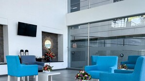 Un vestíbulo moderno con sillas azules, un televisor de pantalla plana y un ventanal grande.