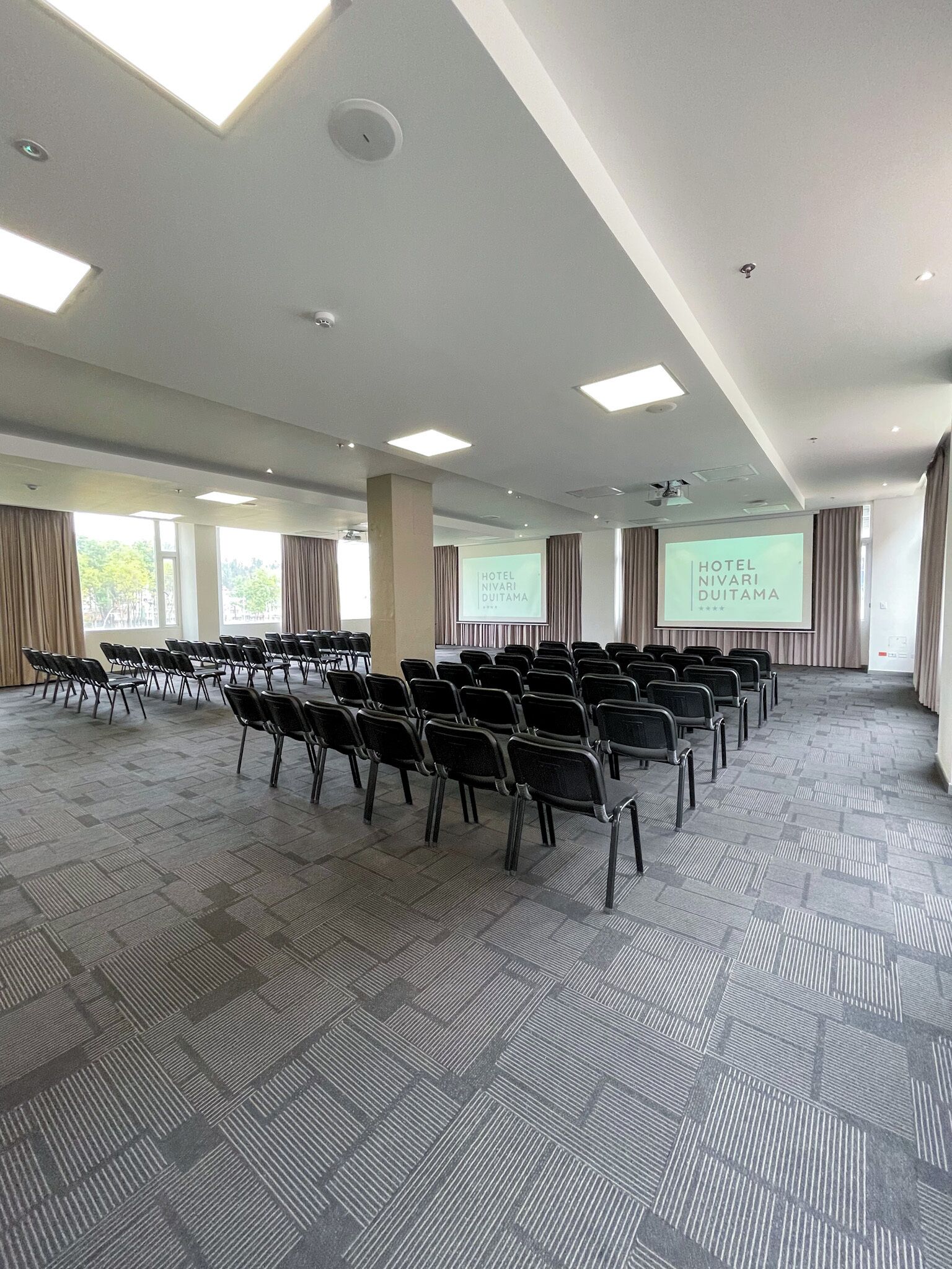 A conference room with rows of chairs, a projection screen, and a large window.
