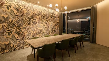 Un comedor moderno con una mesa larga, sillas verdes y vistas a la ciudad a través de amplios ventanales.