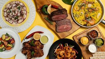 A variety of dishes including seafood, grilled meat, and rice dishes, served on multiple plates and a wooden board.