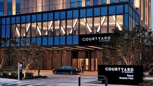 Een moderne hotelentree met een glazen gevel, een bord met 'COURTYARD BY MARRIOTT Seoul Botanic Park' en een parkeersbord.