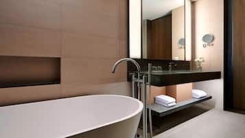 Un baño moderno con una bañera independiente, un lavamanos con encimera oscura y un espejo, y toallas dobladas con cuidado.