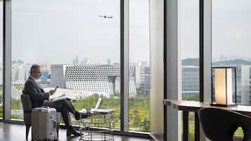 A modern hotel room with large windows, a view of the cityscape, a laptop, and a suitcase.