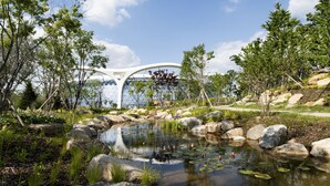 Een modern gebouw met een bijzondere, gebogen dakconstructie, omringd door een natuurlandschap met een vijver en rotsen.
