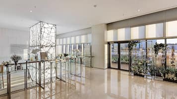 Een ruime lobby met glazen balustrade, een decoratieve glazen scheidingswand en stadszicht door grote ramen.