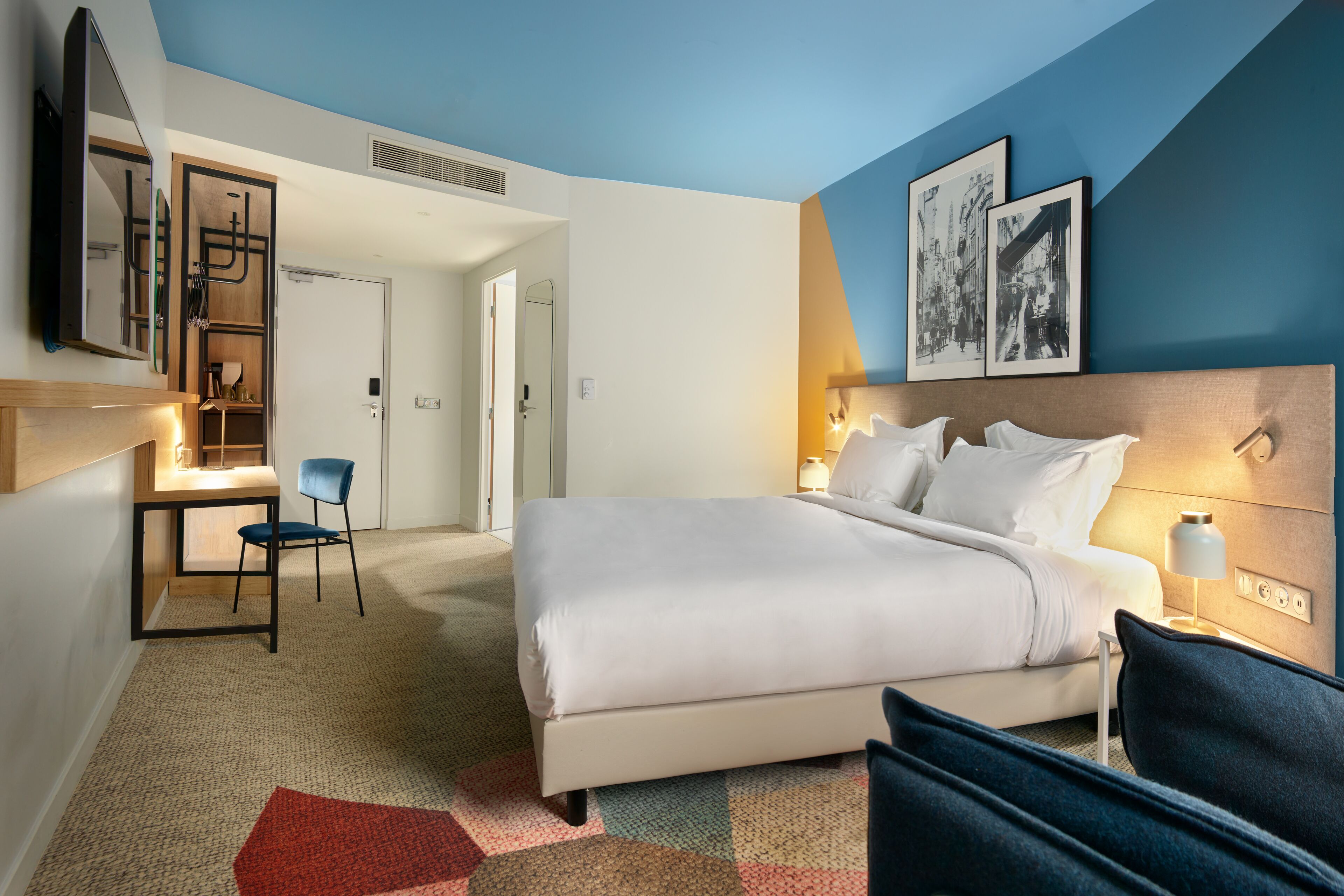 A hotel room with a large bed, a desk with a chair, and a view of the hallway.
