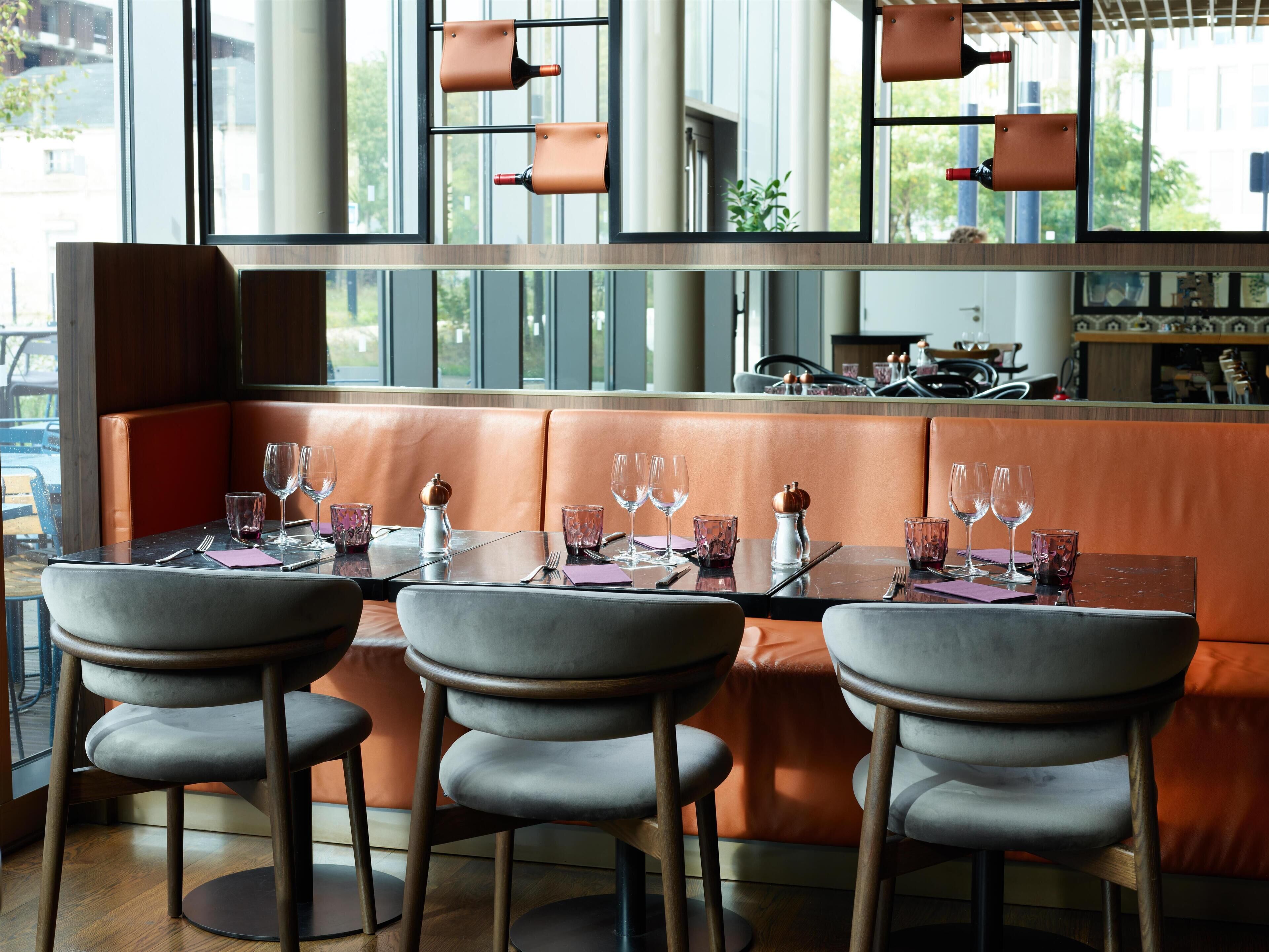 Um restaurante com interior moderno, com assentos de couro, balcão e vista pela janela ampla.