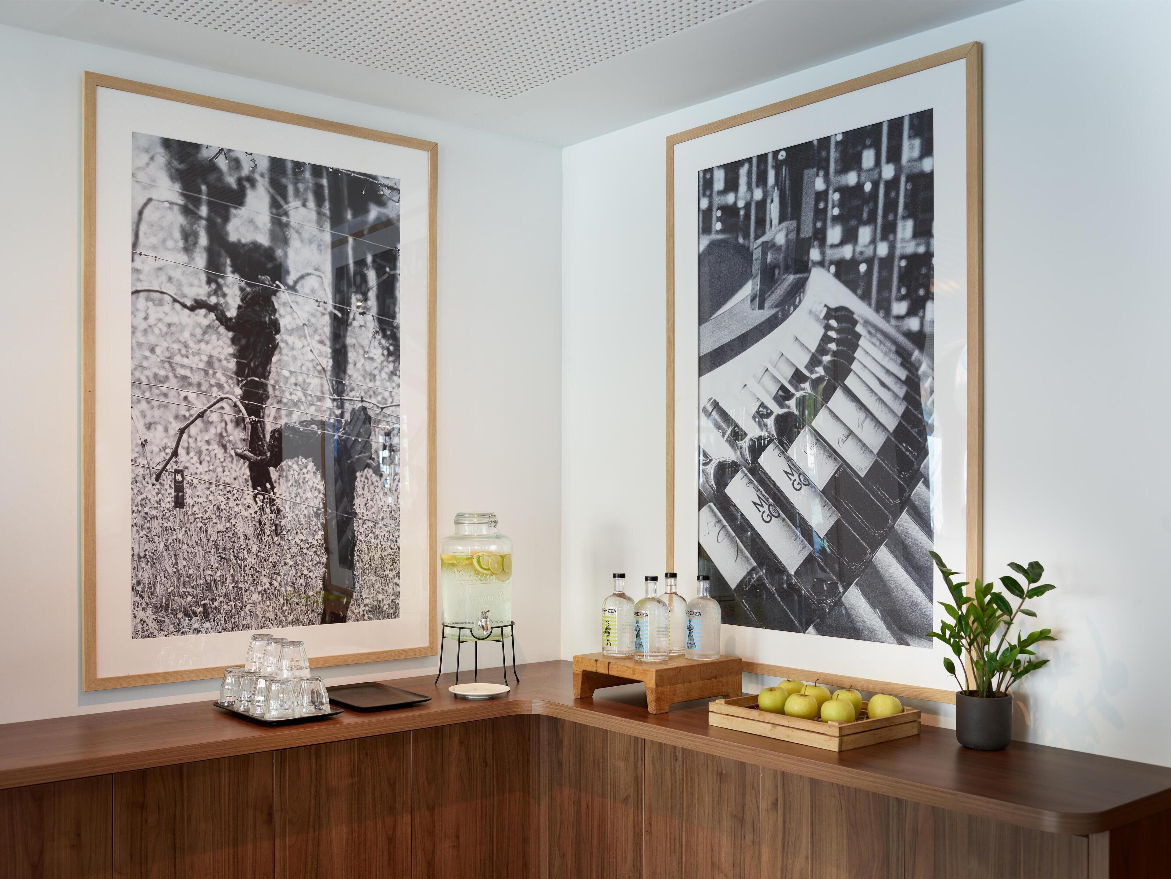 A reception area with two large framed black and white photographs on the wall, a wooden reception desk with a tray of apples and a potted plant, and a small table with a glass jar and bottles.