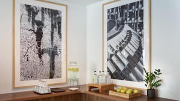 Un espace d’accueil avec deux grandes photographies en noir et blanc encadrées au mur, un comptoir d’accueil en bois sur lequel se trouve un plateau de pommes et une plante en pot, ainsi qu’une petite table avec un bocal en verre et des bouteilles.