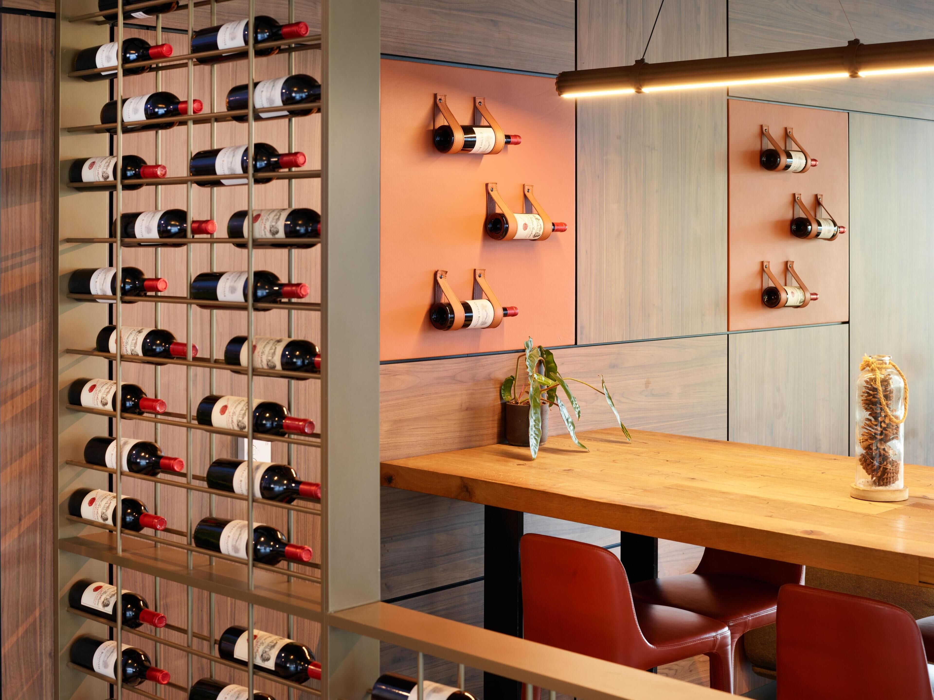 A modern interior with a wine rack, a wooden table, red chairs, and a hanging light fixture.