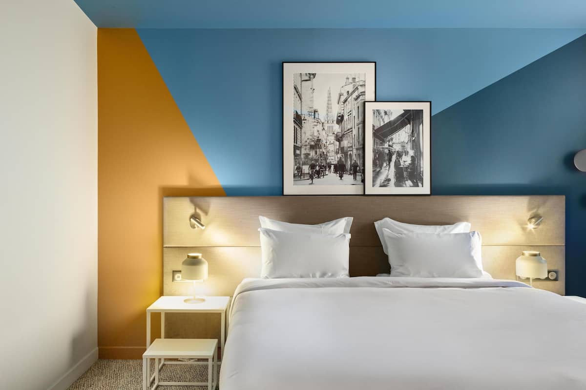 A hotel room with a bed, bedside tables, and two wall-mounted picture frames.