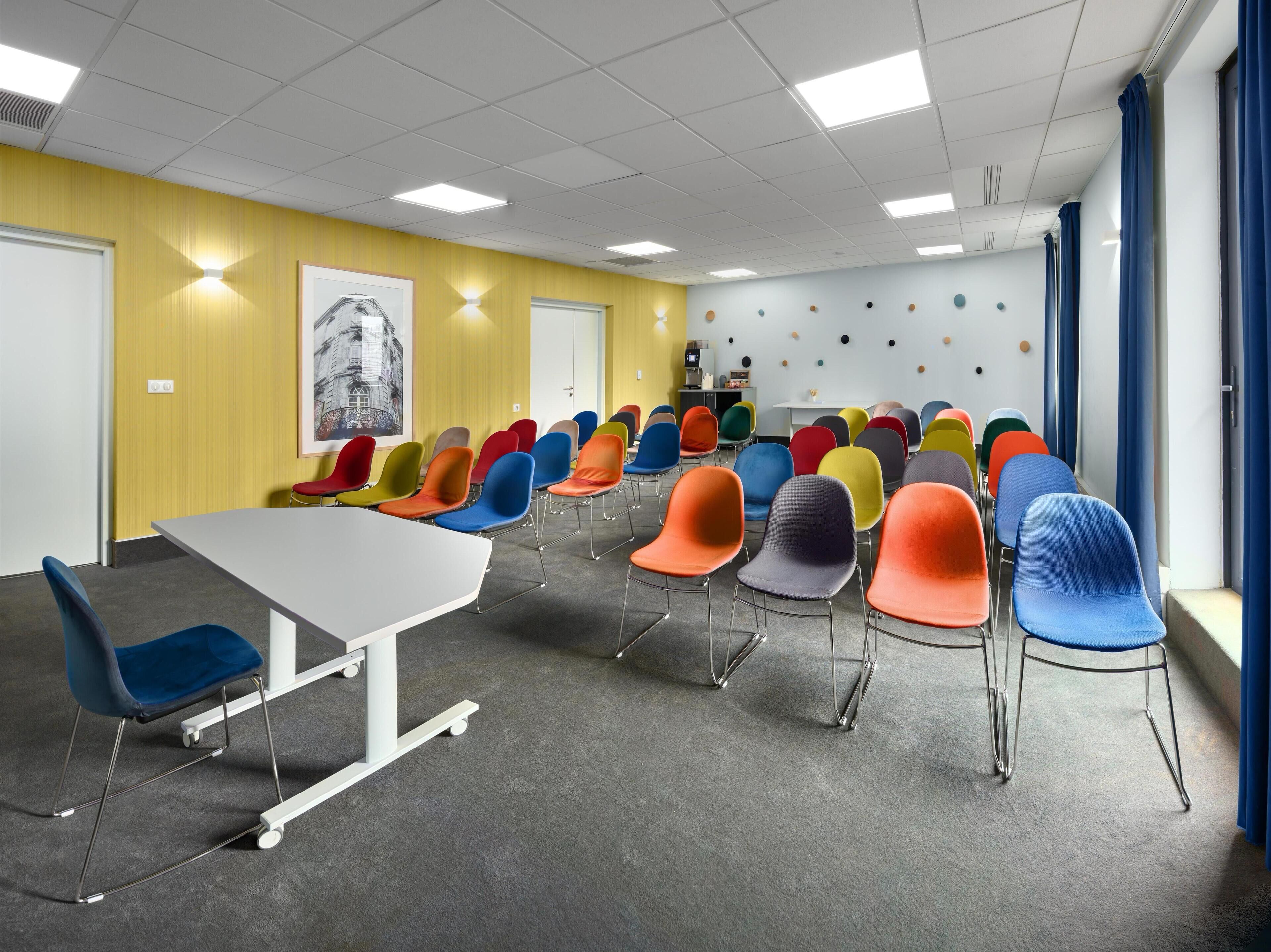 A conference room with a white table and colorful chairs, yellow walls, and a large poster.