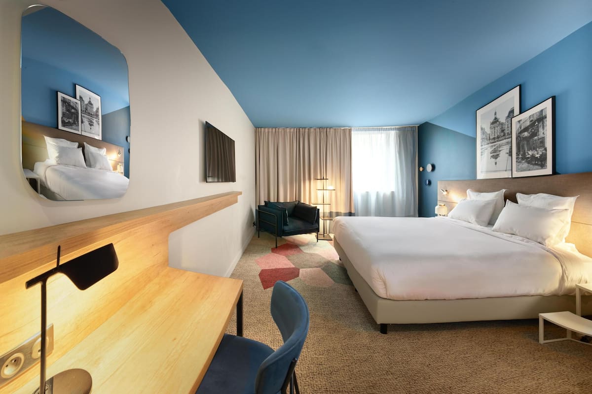 A hotel room with a large bed, a desk, a chair, and a mirror.