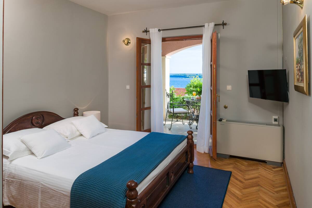 A bedroom with a bed, a TV, and a view of the sea.
