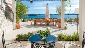 An outdoor patio with a round glass table, wooden chairs, and a view of the sea. - Hvar Boutique Villas (Hvar)