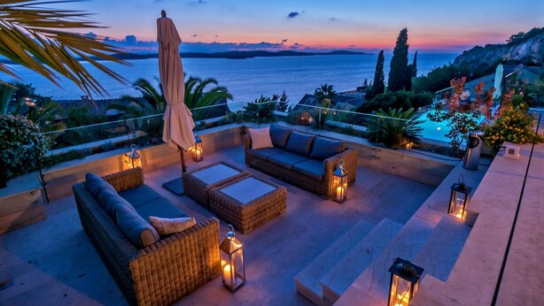 An outdoor seating area with wicker furniture, lanterns, and a view of the sea at dusk. - Hvar Boutique Villas (Hvar)