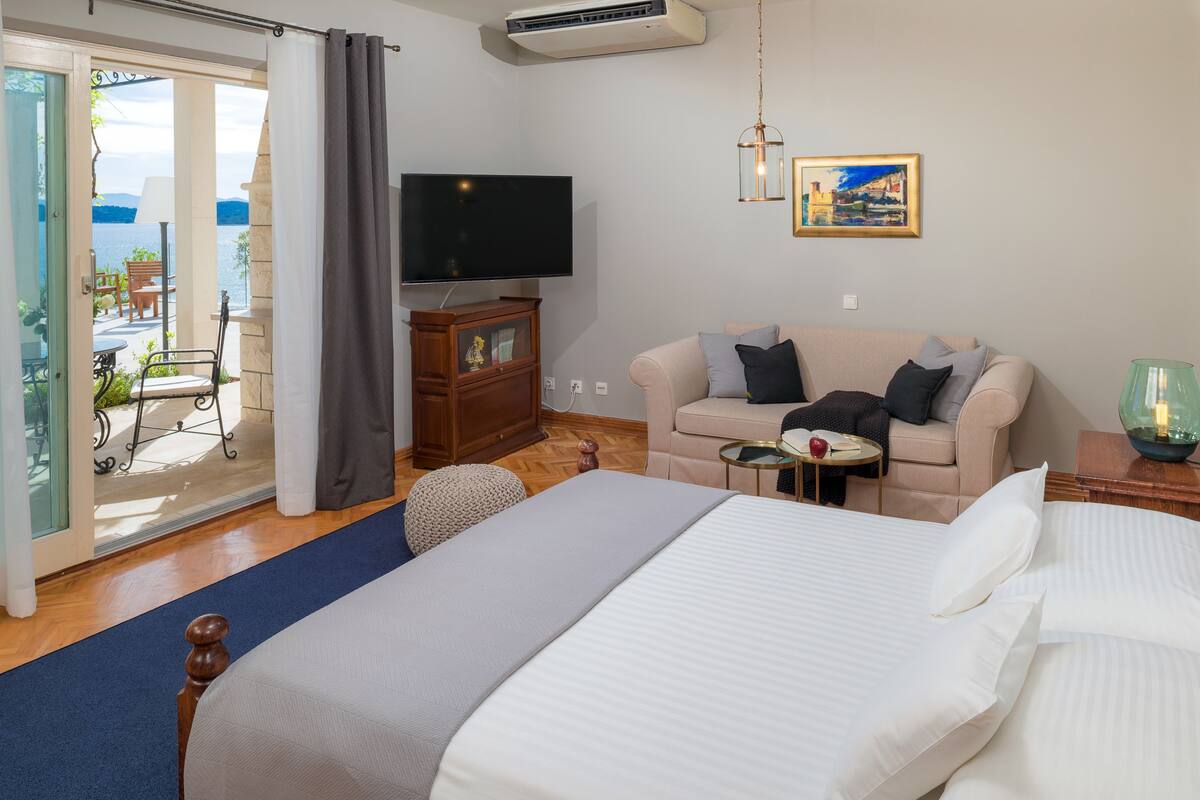 A hotel room with a bed, a sofa, a TV, a small table, and a view of the outdoors.