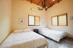 Une chambre avec deux lits, un ventilateur de plafond et un climatiseur fixé au mur.