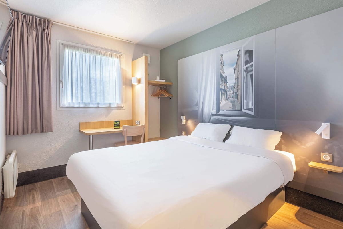 Ein Hotelzimmer mit einem großen Bett, einem Schreibtisch, einem Sessel und einem Bild an der Wand.