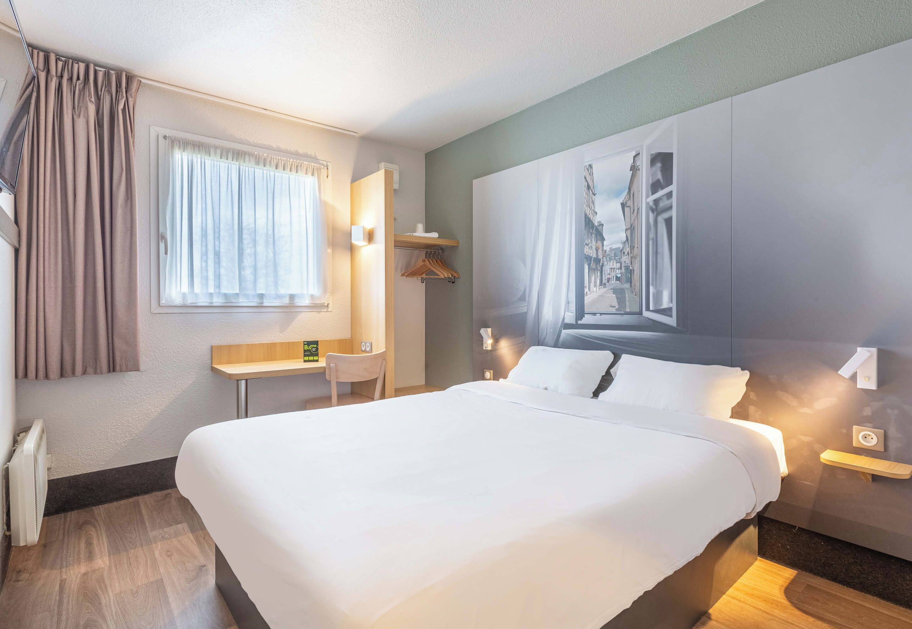 A hotel room with a large bed, a desk, a chair, and a painting on the wall.