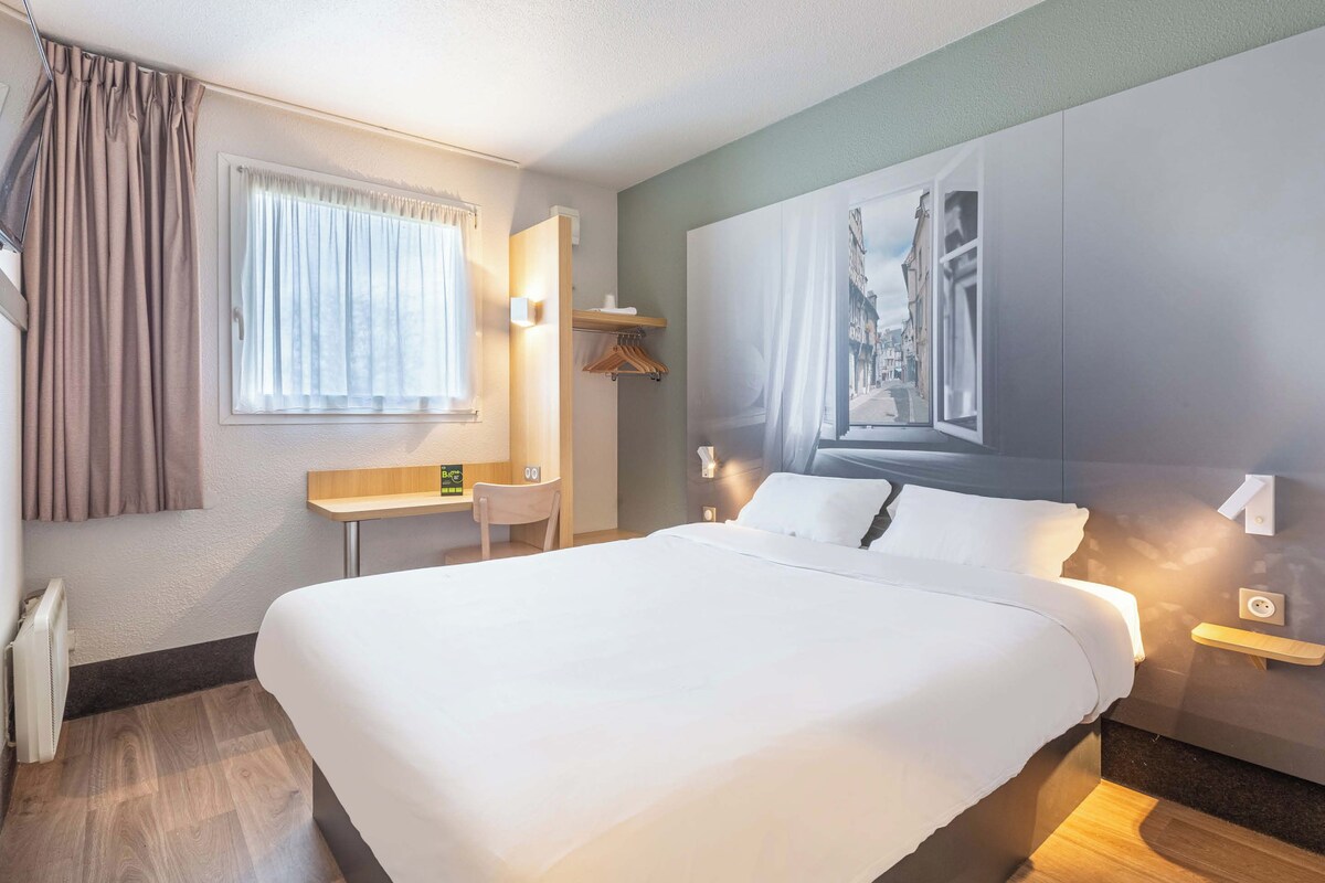 Habitación de hotel con una cama grande, un escritorio, una silla y un cuadro en la pared.