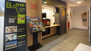 Een hotel receptie met een receptiebalie, een bord met 'B&me' programma en informatiebrochures.