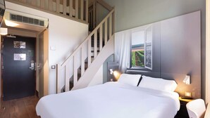 Een hotelkamer met een groot bed, een trap, een raam met uitzicht en een wandlamp.
