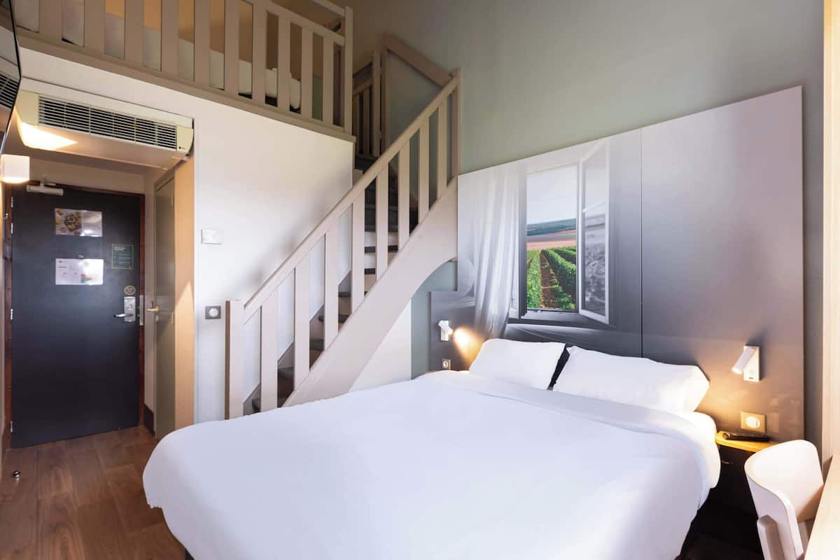 Ein Hotelzimmer mit einem großen Bett, einer Treppe, einem Fenster mit Aussicht und einer Wandleuchte.