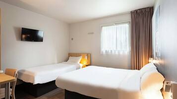 A hotel room with two single beds, a TV mounted on the wall, a desk, and a window with curtains.