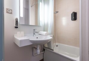 Un baño con lavamanos blanco, espejo, cabezal de ducha y toallero.