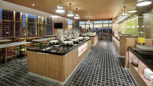 Moderni ravintola, jossa on keskeinen saareke, puinen katto ja suuret ikkunat, joista avautuu näkymä kaupunkiin.