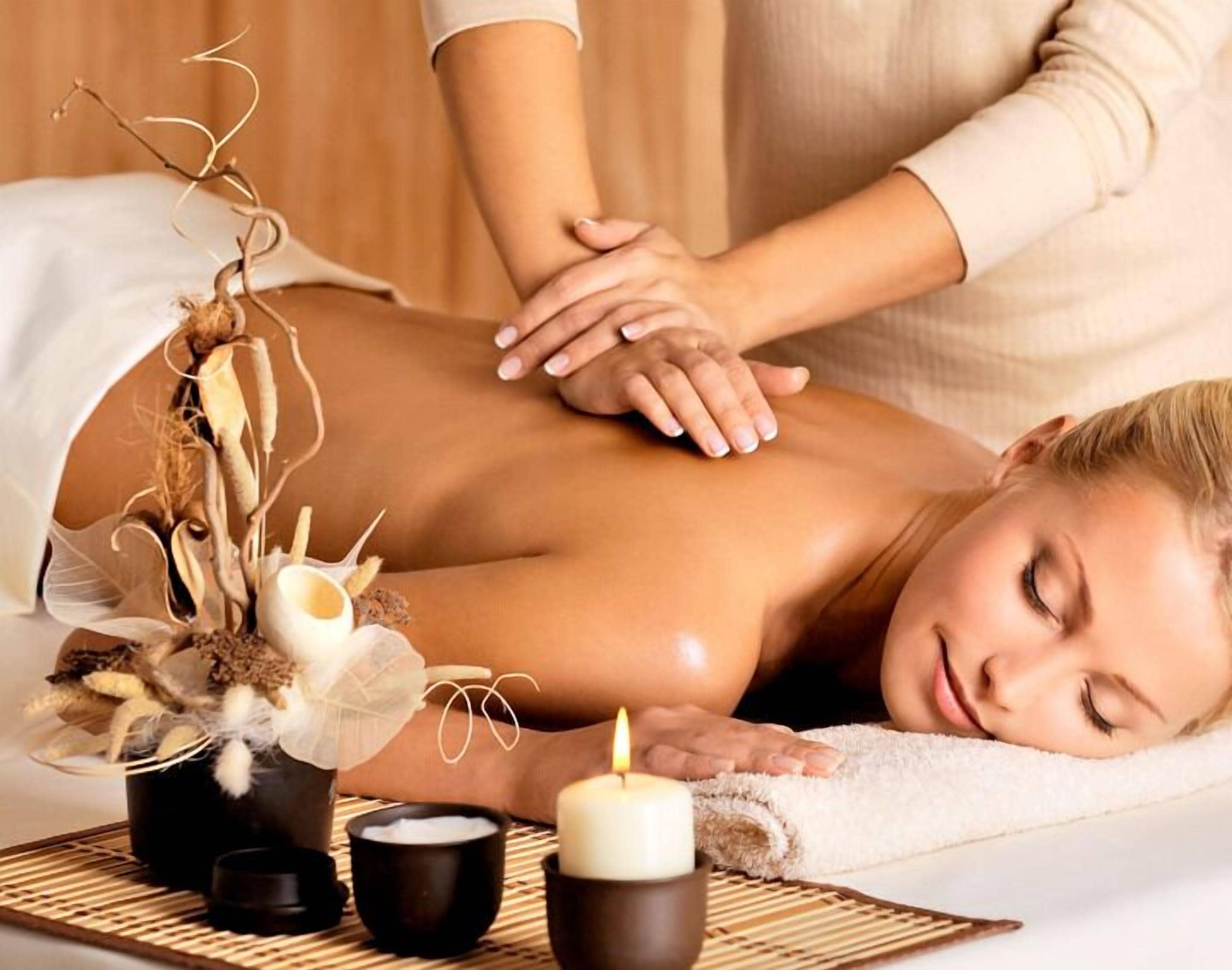 Un ambiente de spa con una persona recibiendo un masaje en la espalda, una vela y elementos decorativos sobre una mesa.