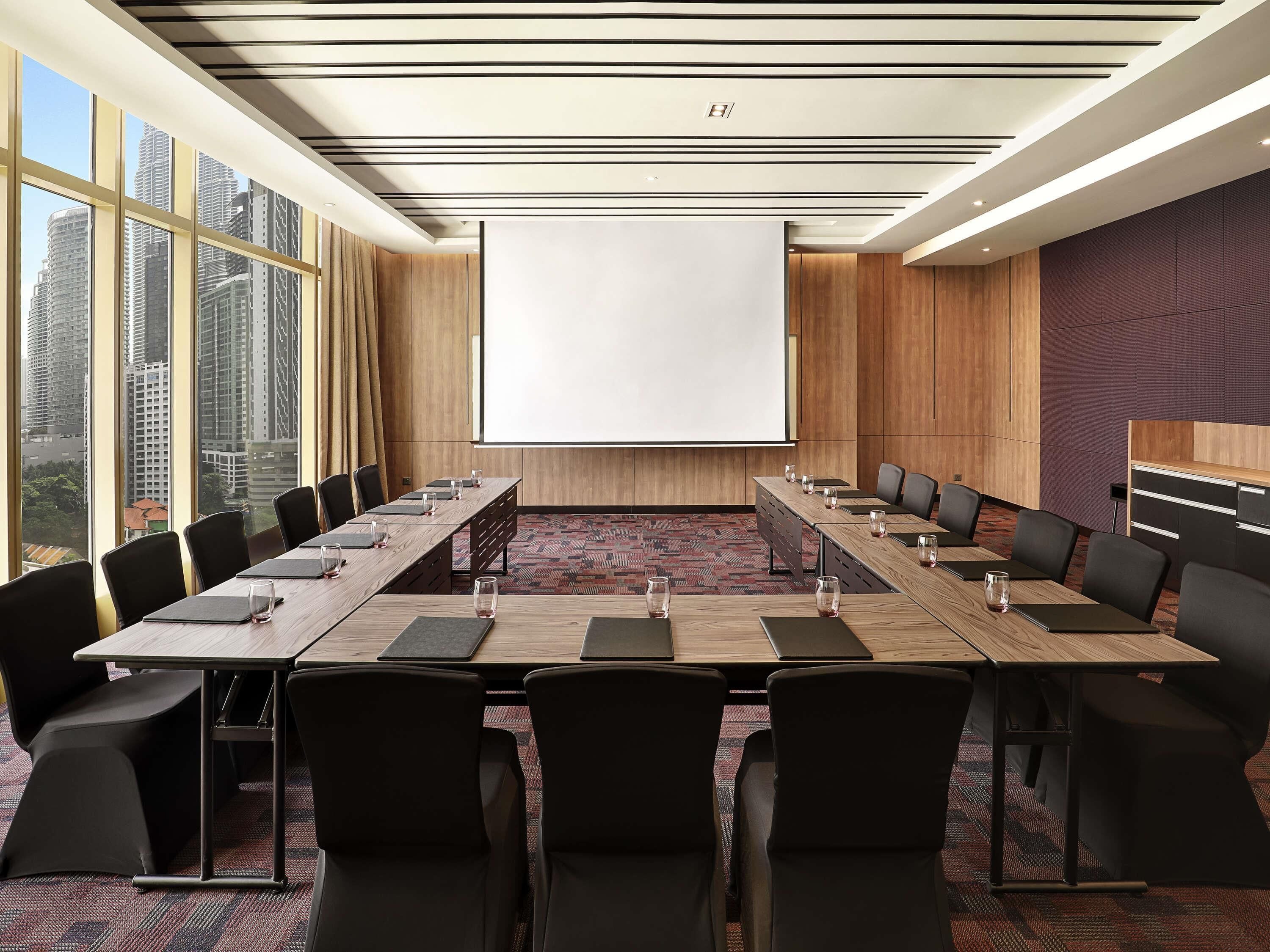 A conference room with a large table, chairs, a projector screen, and a view of tall buildings.