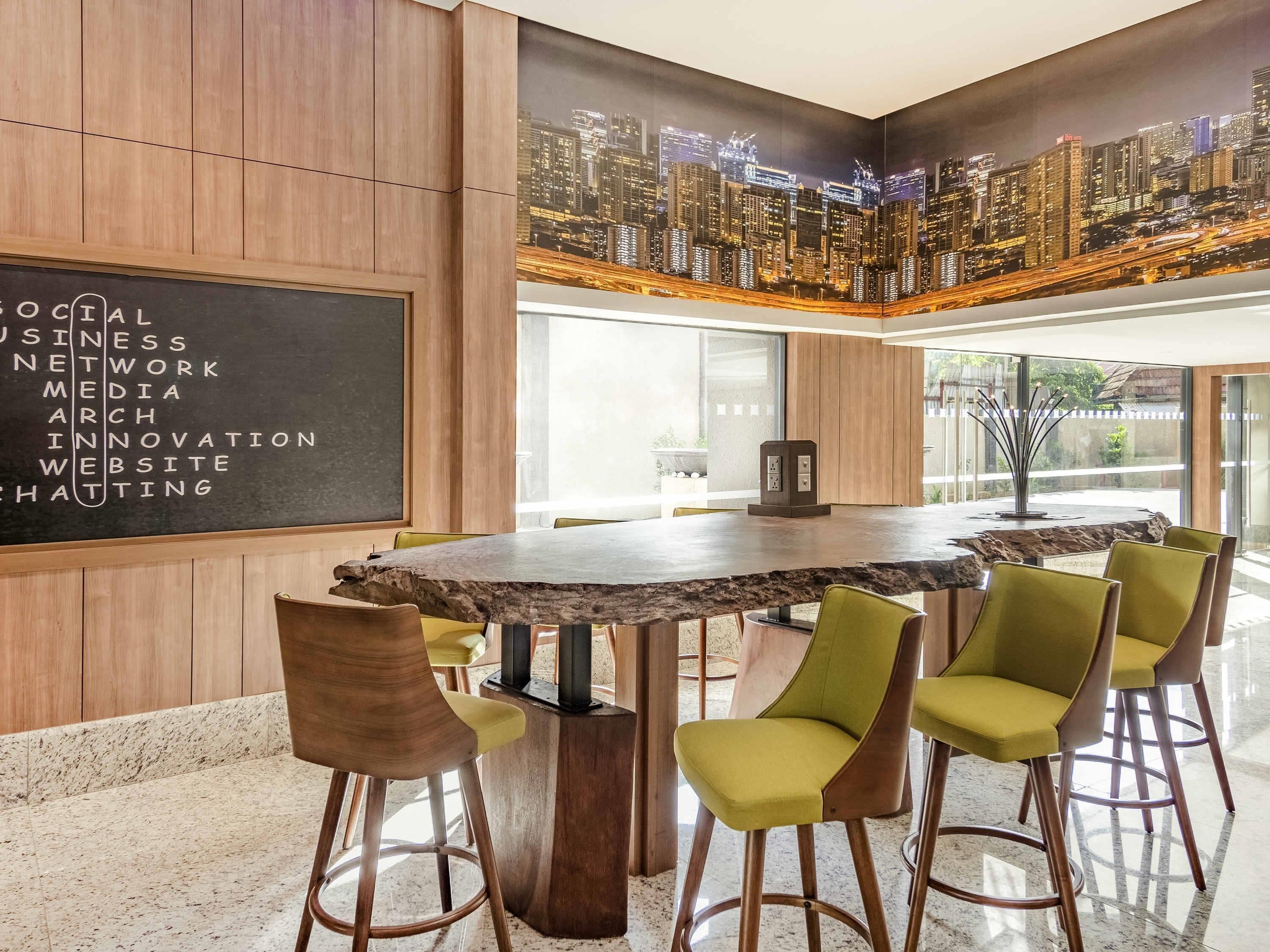 Une salle de conférence moderne, dotée d’une grande table, de chaises vertes et d’une fresque murale représentant un paysage urbain.