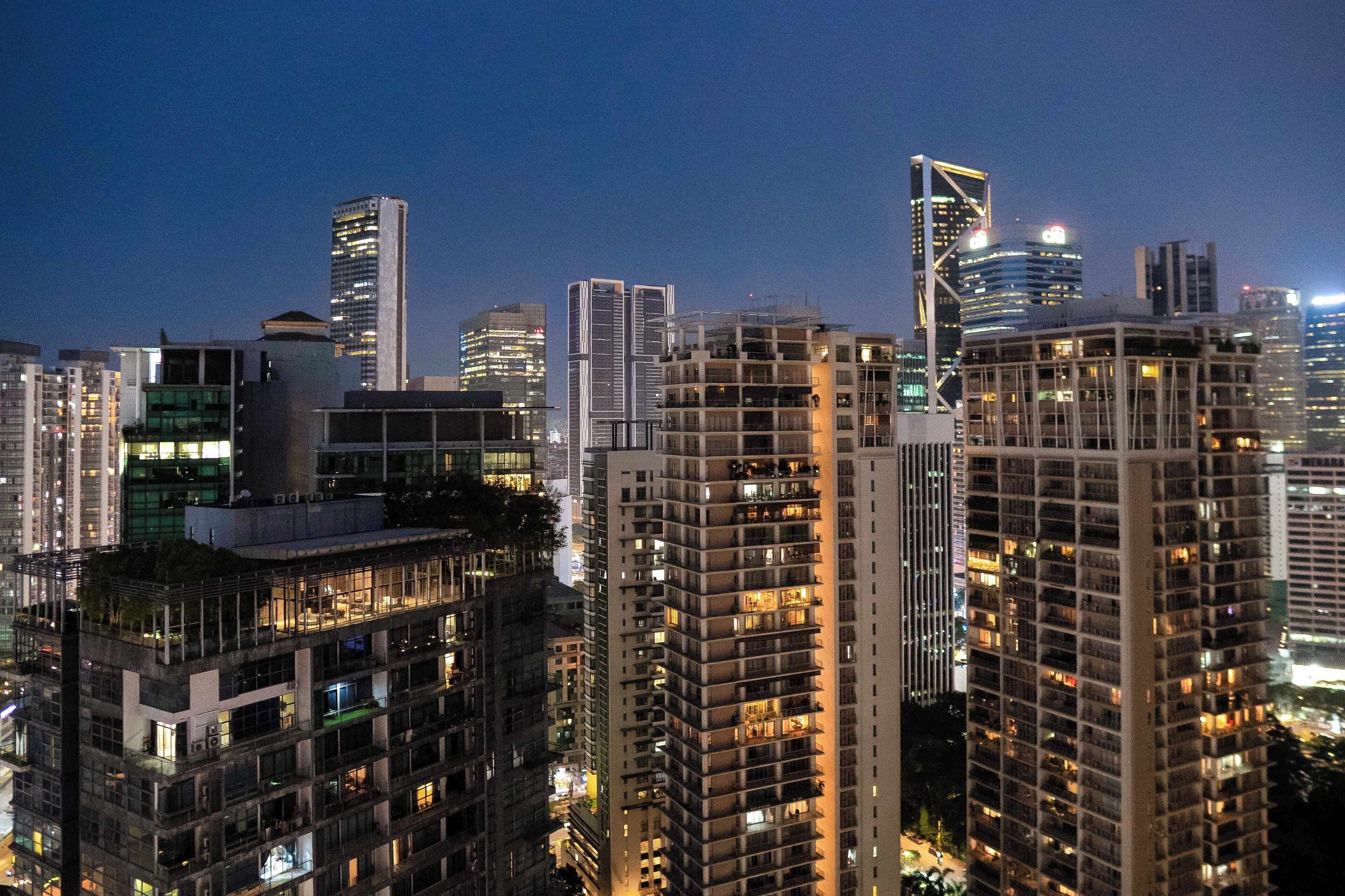 Une vue urbaine avec de hauts immeubles, dont certains sont dotés de balcons et de grandes fenêtres, sous un ciel crépusculaire.