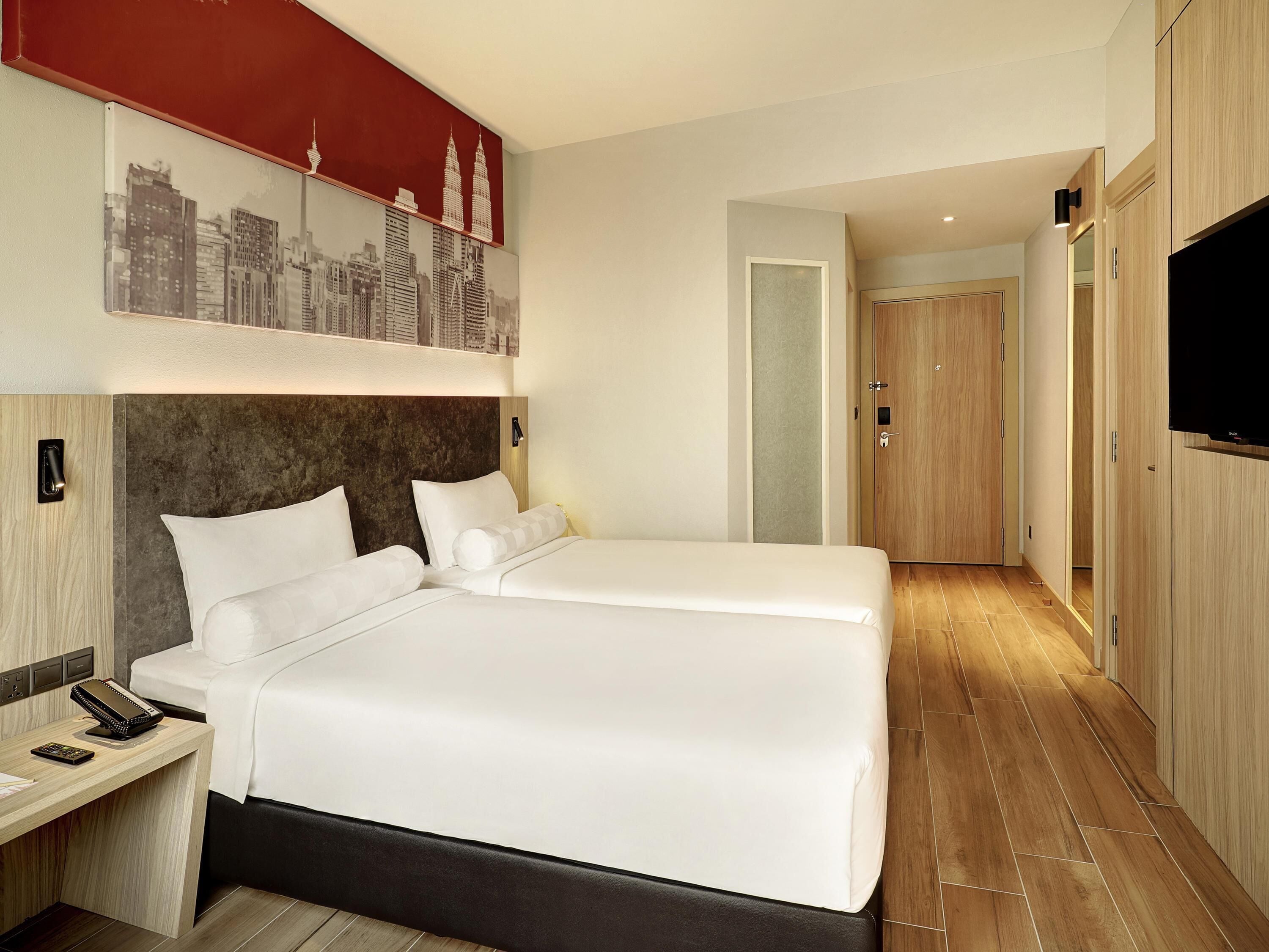 Une chambre d’hôtel avec un grand lit, une table de chevet avec un téléphone et un téléviseur fixé au mur.