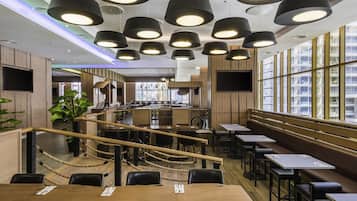 A modern restaurant with multiple dining areas, including a bar and seating with a view of the city.
