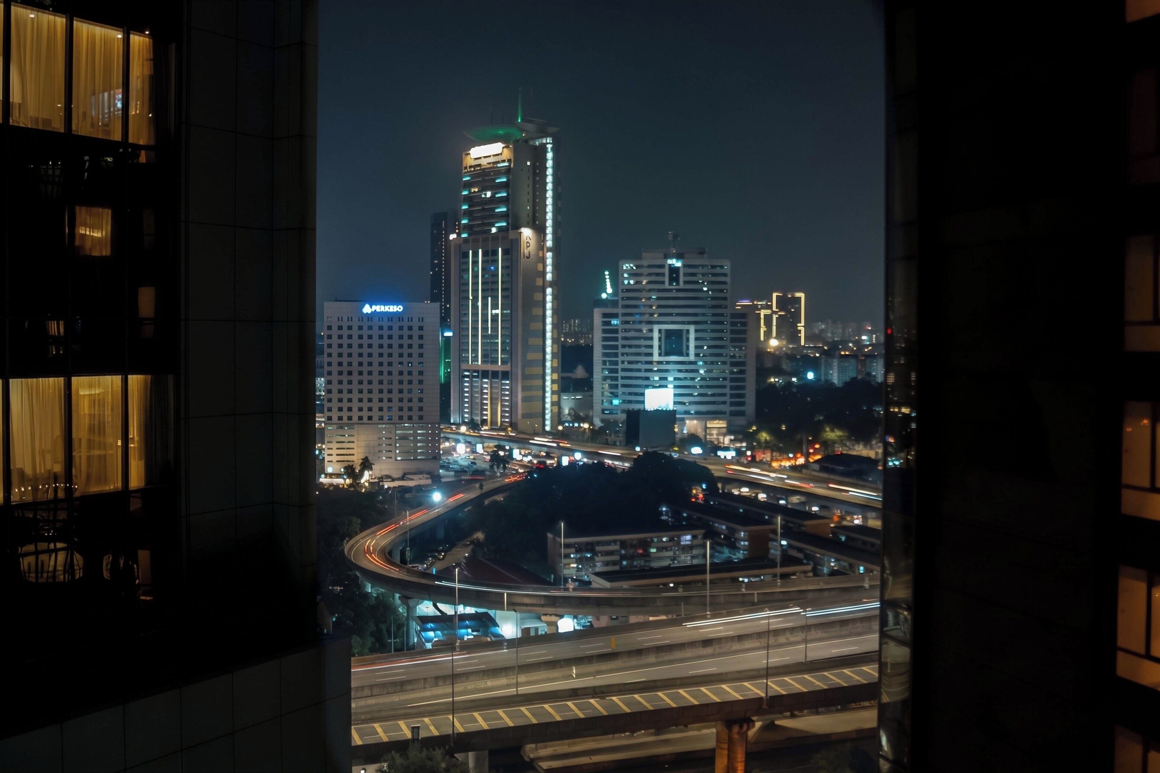 A nighttime cityscape with illuminated buildings and a highway.